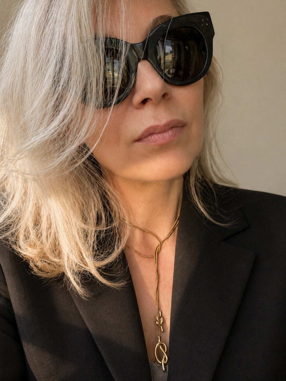 Time4Me long gold stainless steel necklace with asymmetric knots worn by a woman in a black blazer and sunglasses