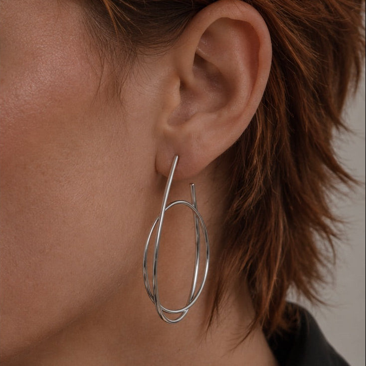 Time4Me silver hoop earrings with an intertwined ring design worn on a woman's ear, made of stainless steel.