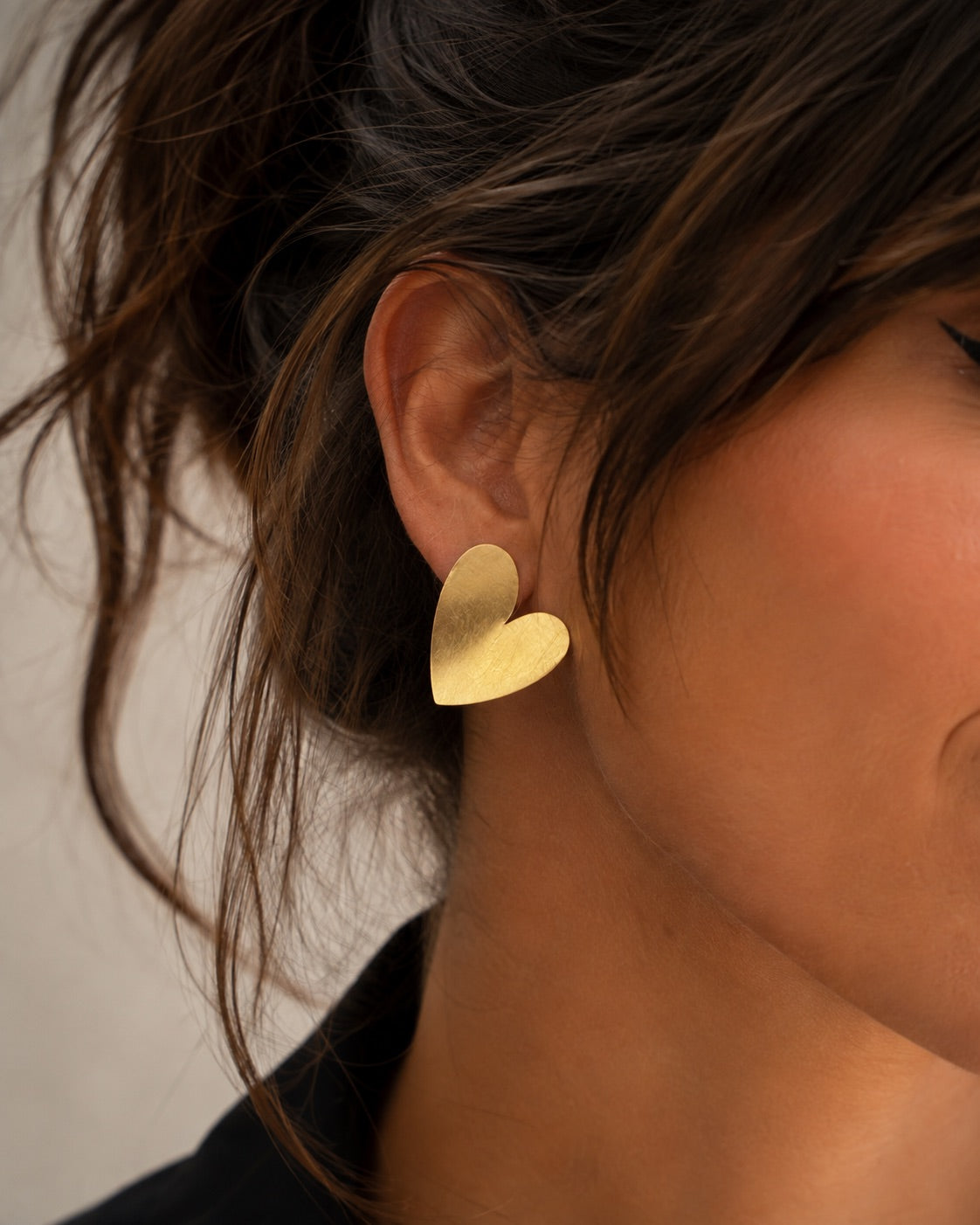 Time4Me gold-tone heart-shaped earrings with a brushed finish worn by a woman with a messy bun hairstyle