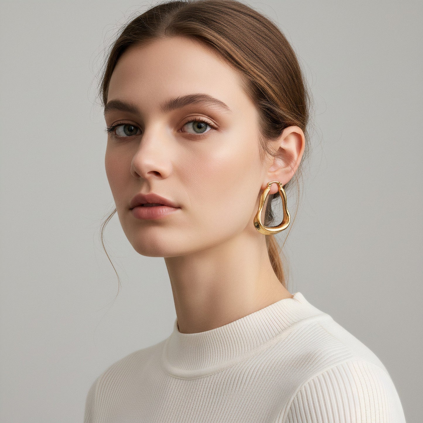 Time4Me gold brushed organic shaped stainless steel hoop earrings worn by a woman in a white ribbed top
