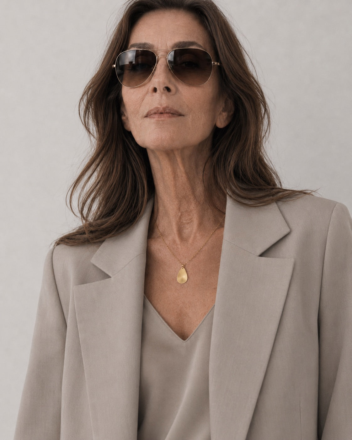 Time4Me gold chain necklace with a brushed teardrop pendant worn by a woman in a beige blazer and sunglasses.