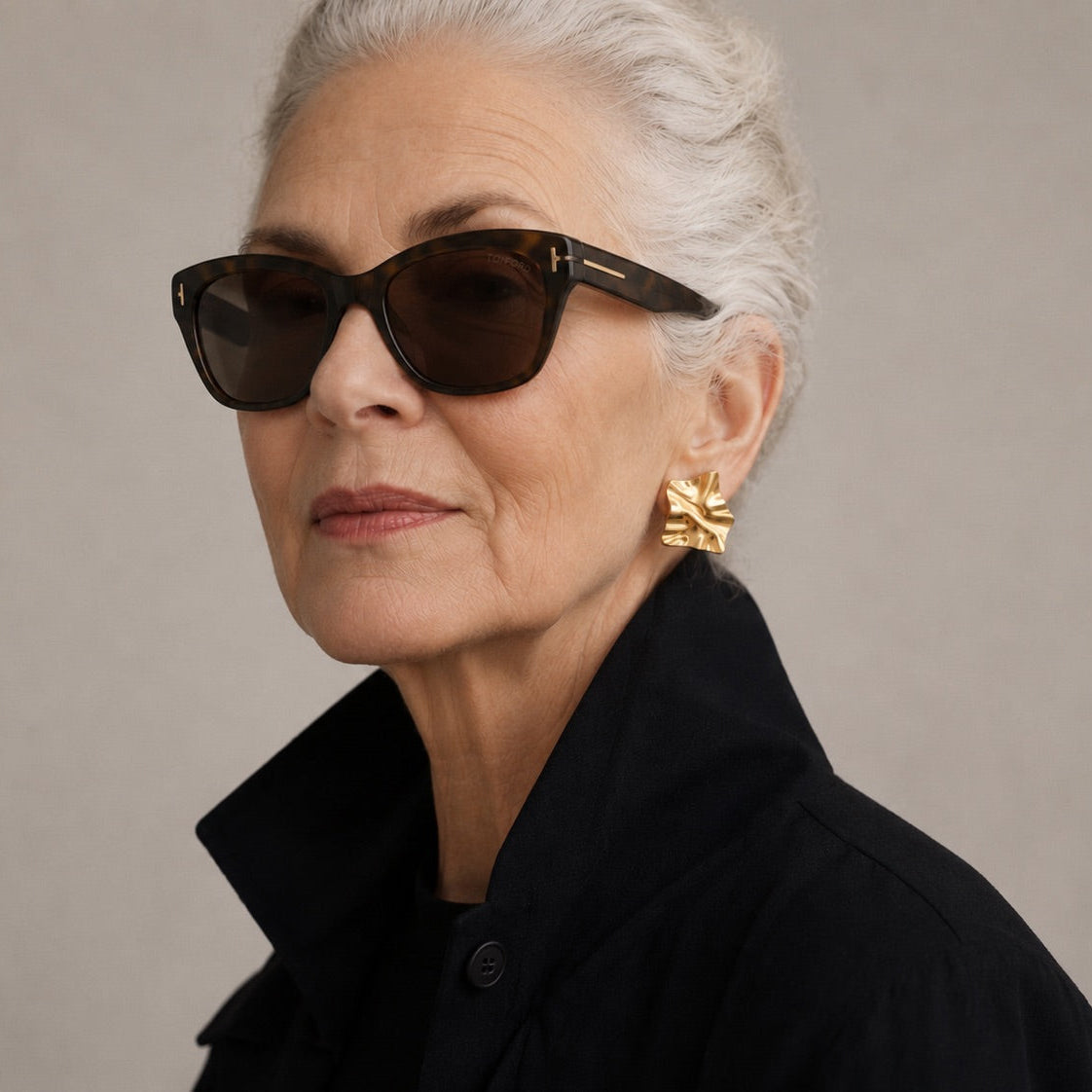Time4Me gold geometric earrings with a crinkled texture worn by an elegant woman with grey hair and sunglasses.