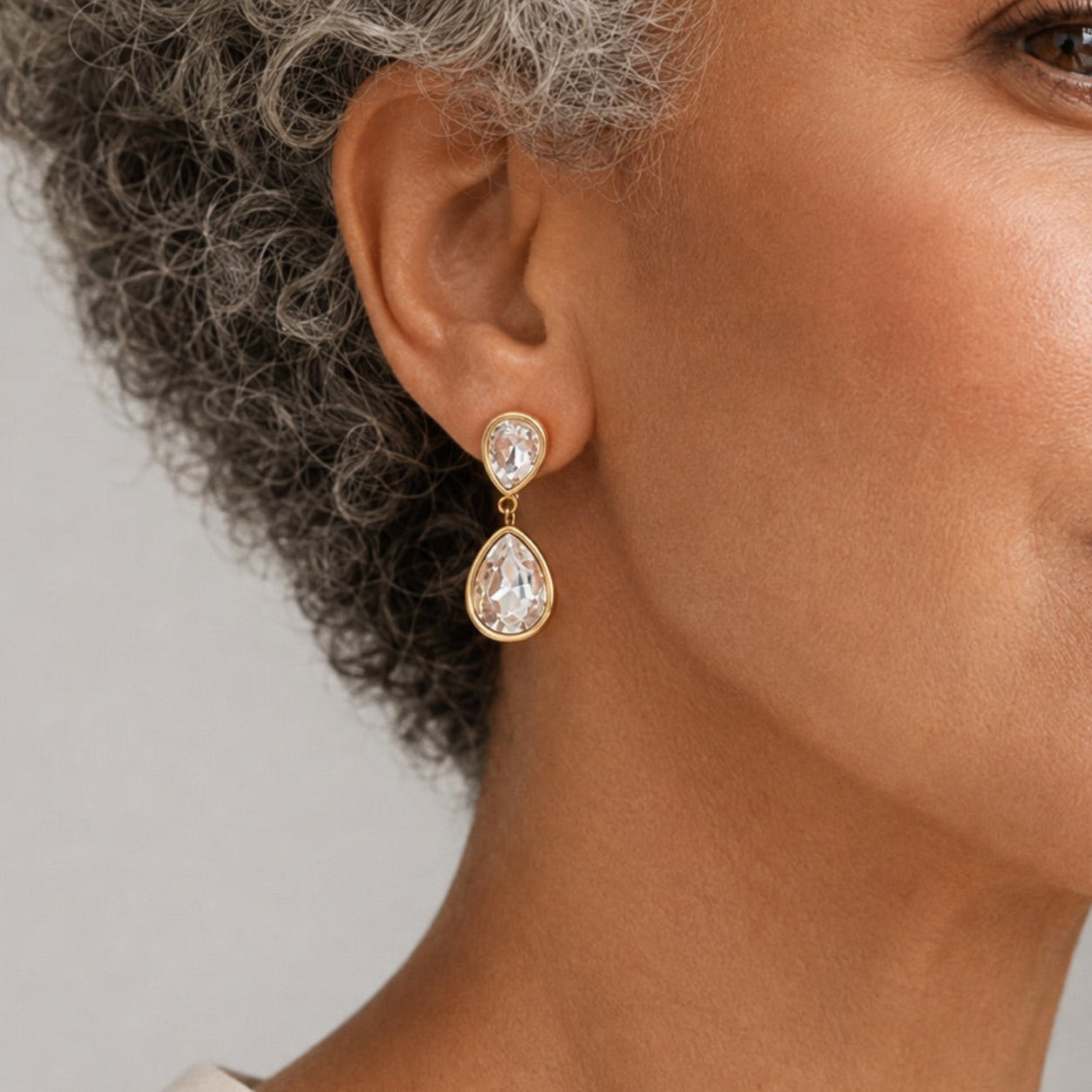 Time4Me long gold-tone stainless steel drop earrings featuring two clear glass teardrop stones worn by a woman