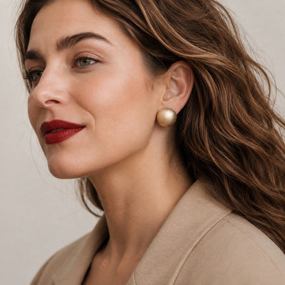 Time4Me gold matte half-sphere stud earrings worn by a woman with wavy hair and red lipstick