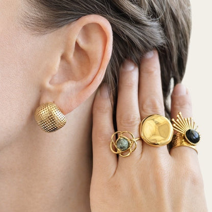 Time4Me gold square perforated earrings worn on a woman's ear, styled with three statement rings on her hand.