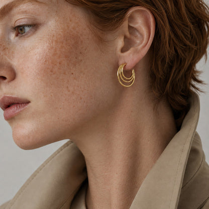 Time4Me gold-tone triple hoop earrings worn by a woman with short red hair and a beige trench coat