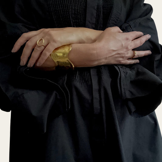 Time4Me adjustable gold wave cuff bracelet with a brushed finish worn on a woman's wrist with a black dress