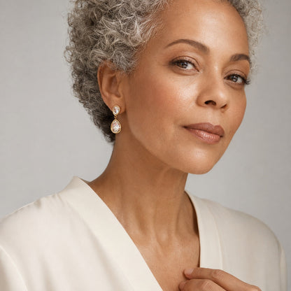 Time4Me long gold stainless steel earrings with two clear glass teardrop pendants worn by a mature woman