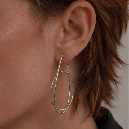 Time4Me silver hoop earrings with an intertwined ring design worn on a woman's ear, made of stainless steel.